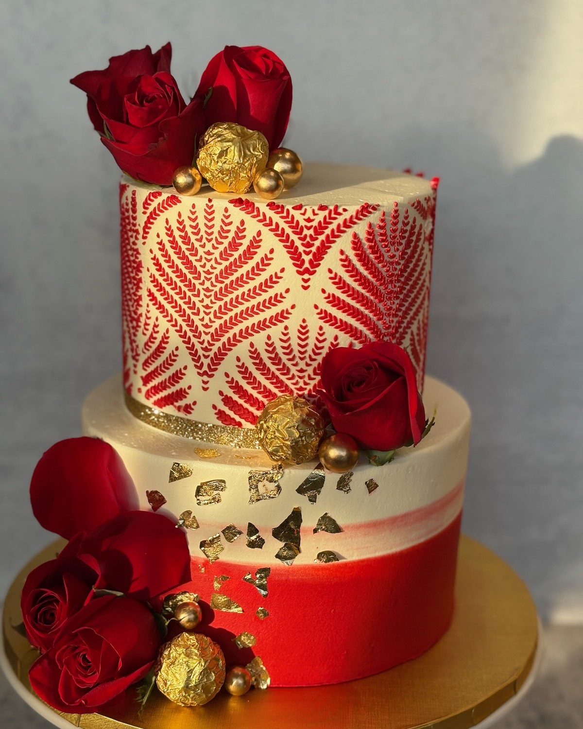 Two-tier red and gold henna-inspired cake with roses and Ferrero Rocher