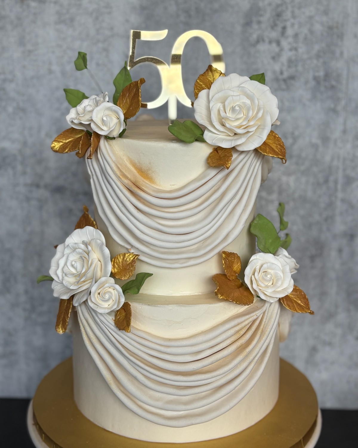 Elegant two-tier 50th anniversary cake with white fondant draping and gold accents